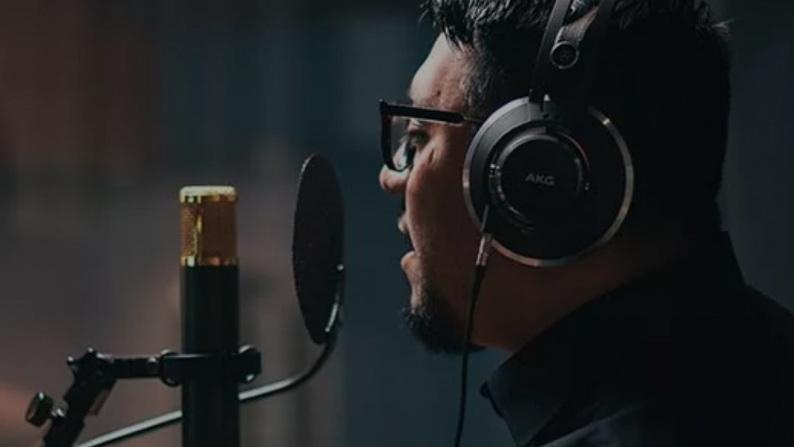 A young man wearing headphones singing into a microphone in a studio