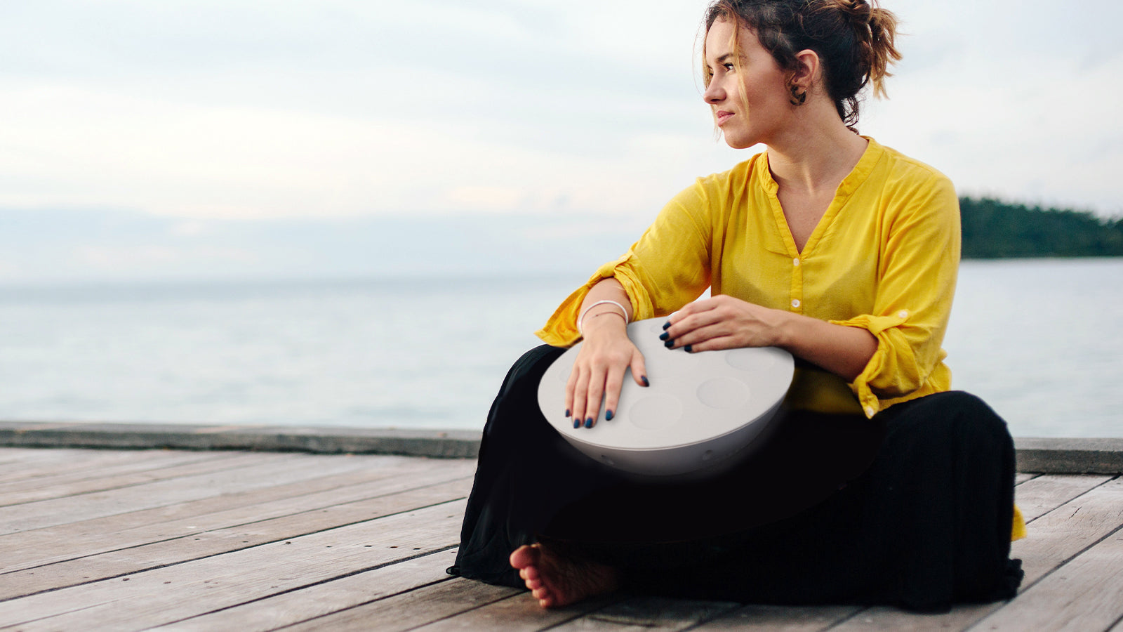 Woman sitting cross-legged on dock and playing Roland Mood Pan