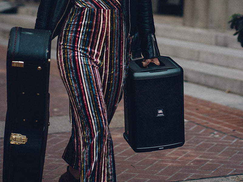 Image of person carrying a guitar case and JBL portable speaker