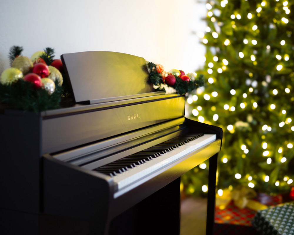 Kawai digital piano decorated with holiday ornaments, in front of a Christmas tree and wrapped gifts