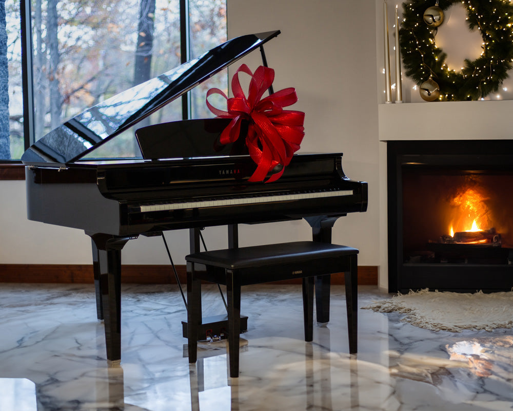 Image of Yamaha digital grand piano with a bow on it, in front of a festive fireplace.