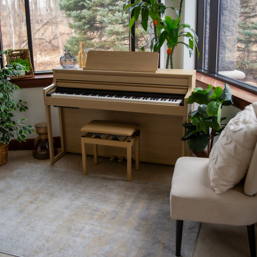 Roland HP704 Digital Piano - Light Oak in a room with plants and a window
