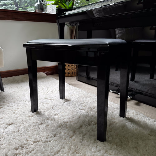 A Kawai piano bench with a padded black seat cushion, positioned on a white shag rug next to a Kawai NOVUS NV6 Hybrid Upright Piano.