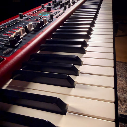 Close-up of a Nord Electro 7 with black and white keys, photographed in a dim indoor setting.