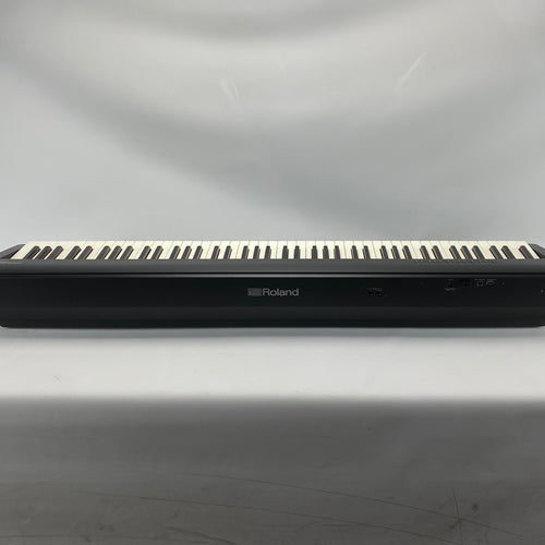 A Roland digital piano keyboard, shown from the back against a light gray draped fabric background.