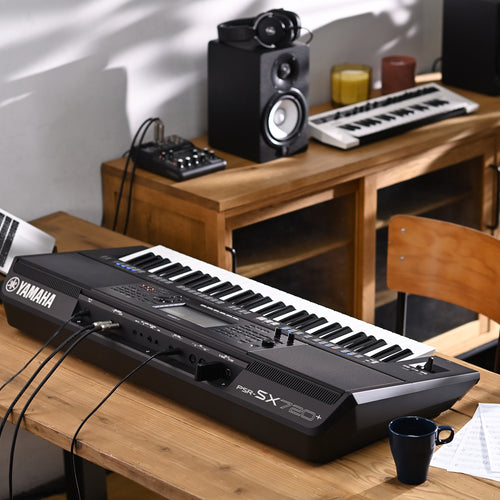 Yamaha keyboard on a wooden desk with laptop, speakers, and other music equipment.