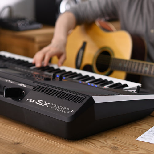 Keyboard on a wooden table with a person playing guitar in the background