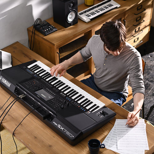 Person playing a Yamaha keyboard in a home setting with musical instruments around