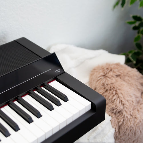 Close up of a Yamaha P-S500B Digital Piano with L-300B Stand and LP-1B Triple Pedal - Black with a soft pillow and green plant in the background
