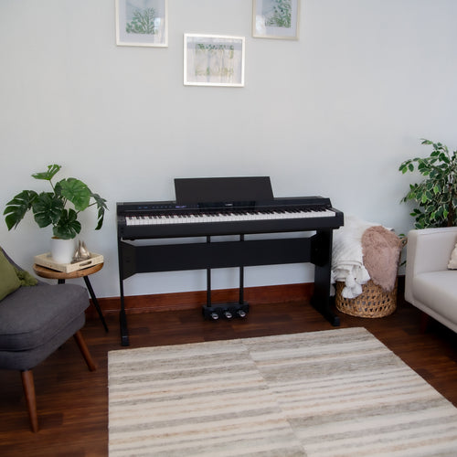 Yamaha P-S500B Digital Piano with L-300B Stand and LP-1B Triple Pedal - Black - in a living room with a rug, sofa, and plants.