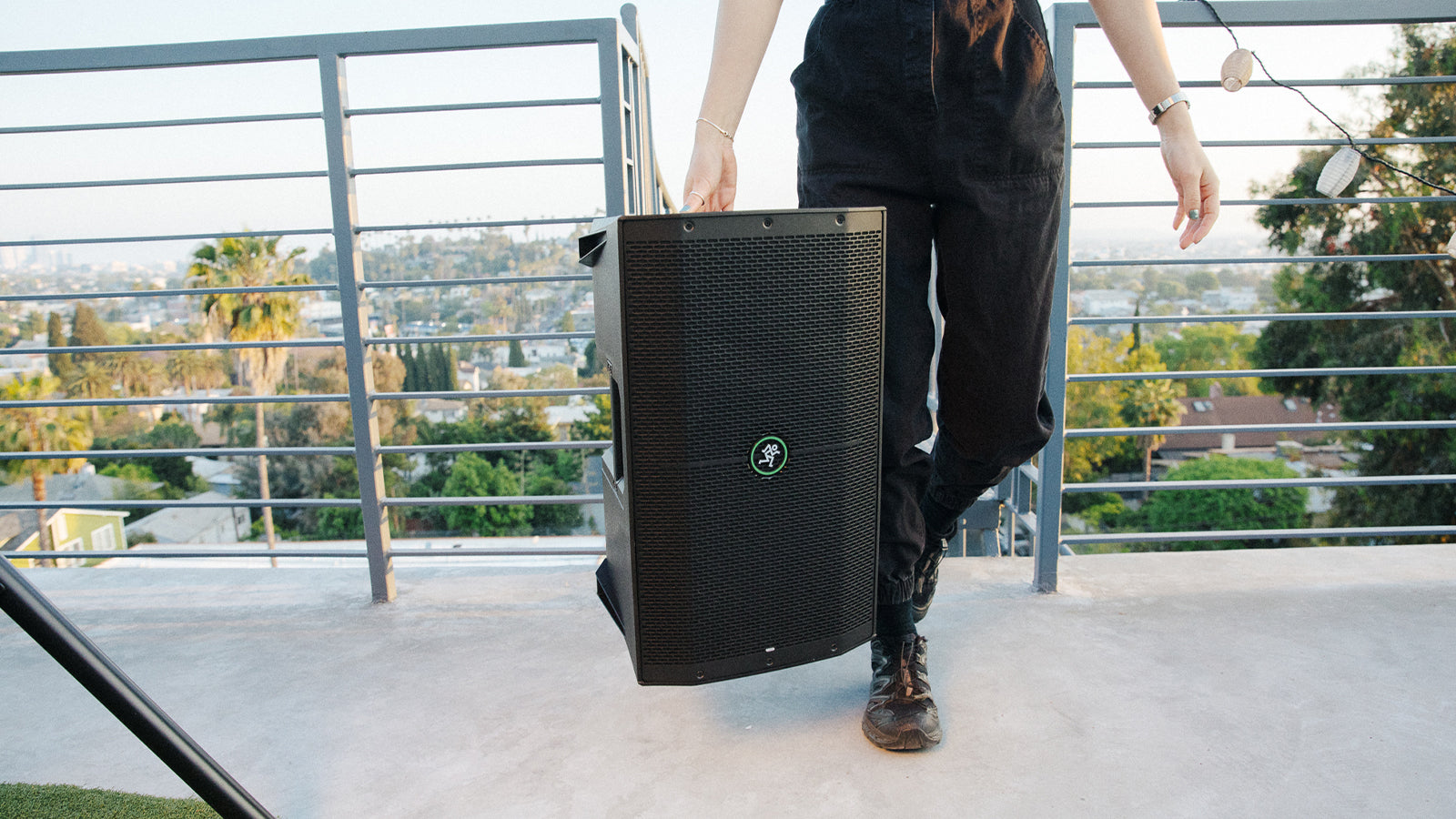 A person carrying a Mackie Thump speaker at an outdoor event