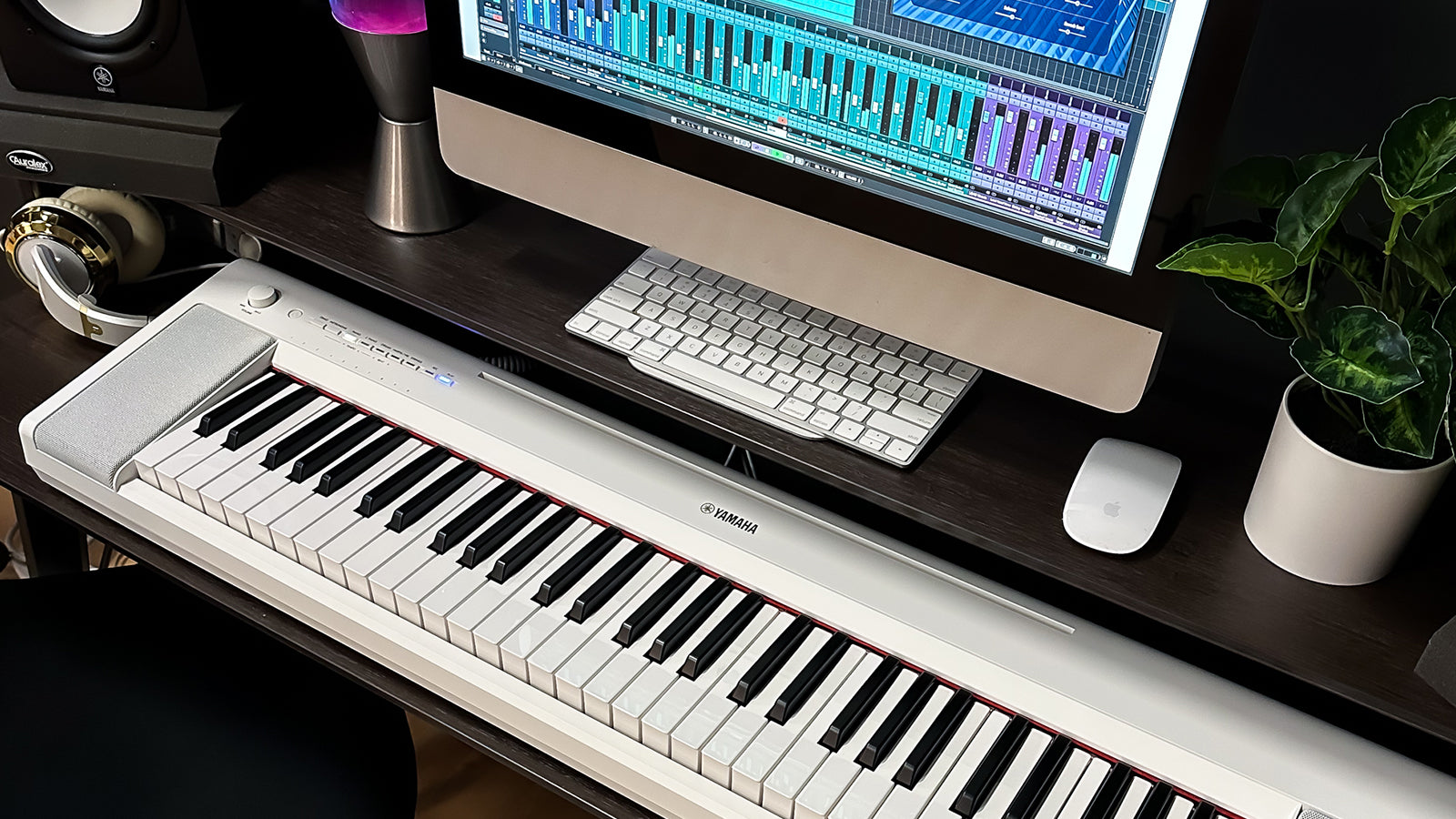 A Yamaha digital piano on a desk in a home studio with Yamaha studio monitors