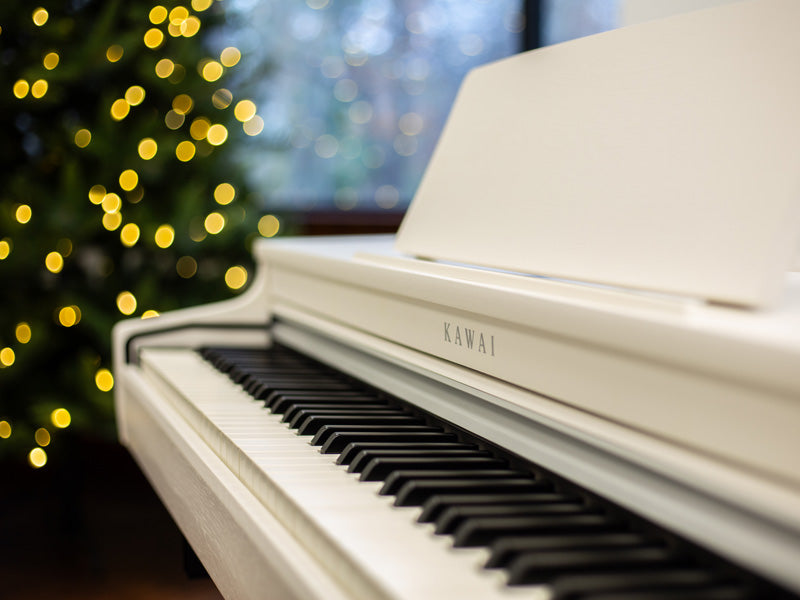 Closeup of a white Kawai CN29 digital piano with Christmas tree in the background.