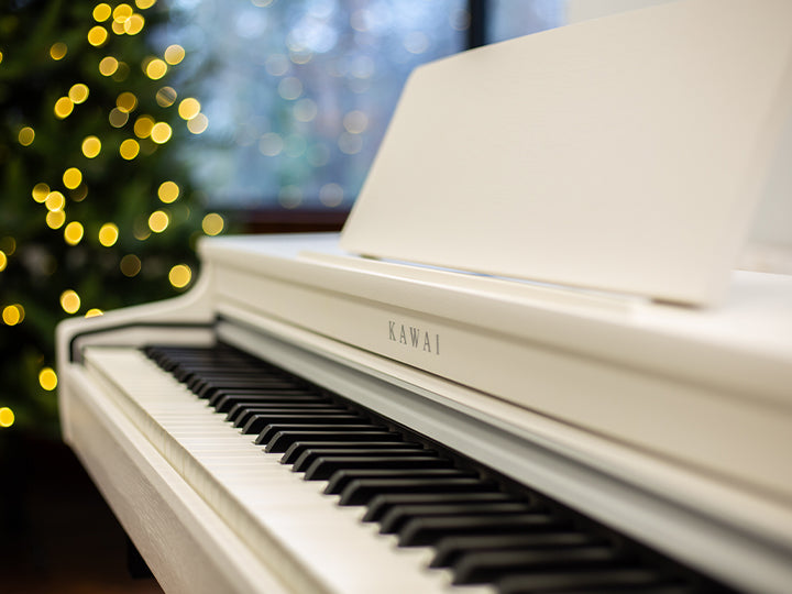A white Kawai CN29 digital piano with a lit tree in the background