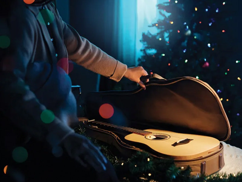 Image of person opening a Taylor guitar case in front of a Christmas tree.