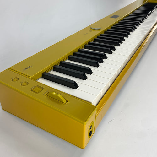 A Casio keyboard in a metallic gold finish, featuring black and white keys, photographed on a light gray background.