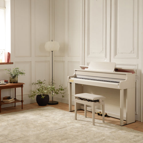 Casio Celviano AP-750 Digital Piano - Grey Beige in a room with light-colored walls, a rug, and a small table with a lamp and plant.