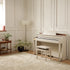 Casio Celviano AP-750 Digital Piano - Grey Beige in a room with light-colored walls, a rug, and a small table with a lamp and plant.