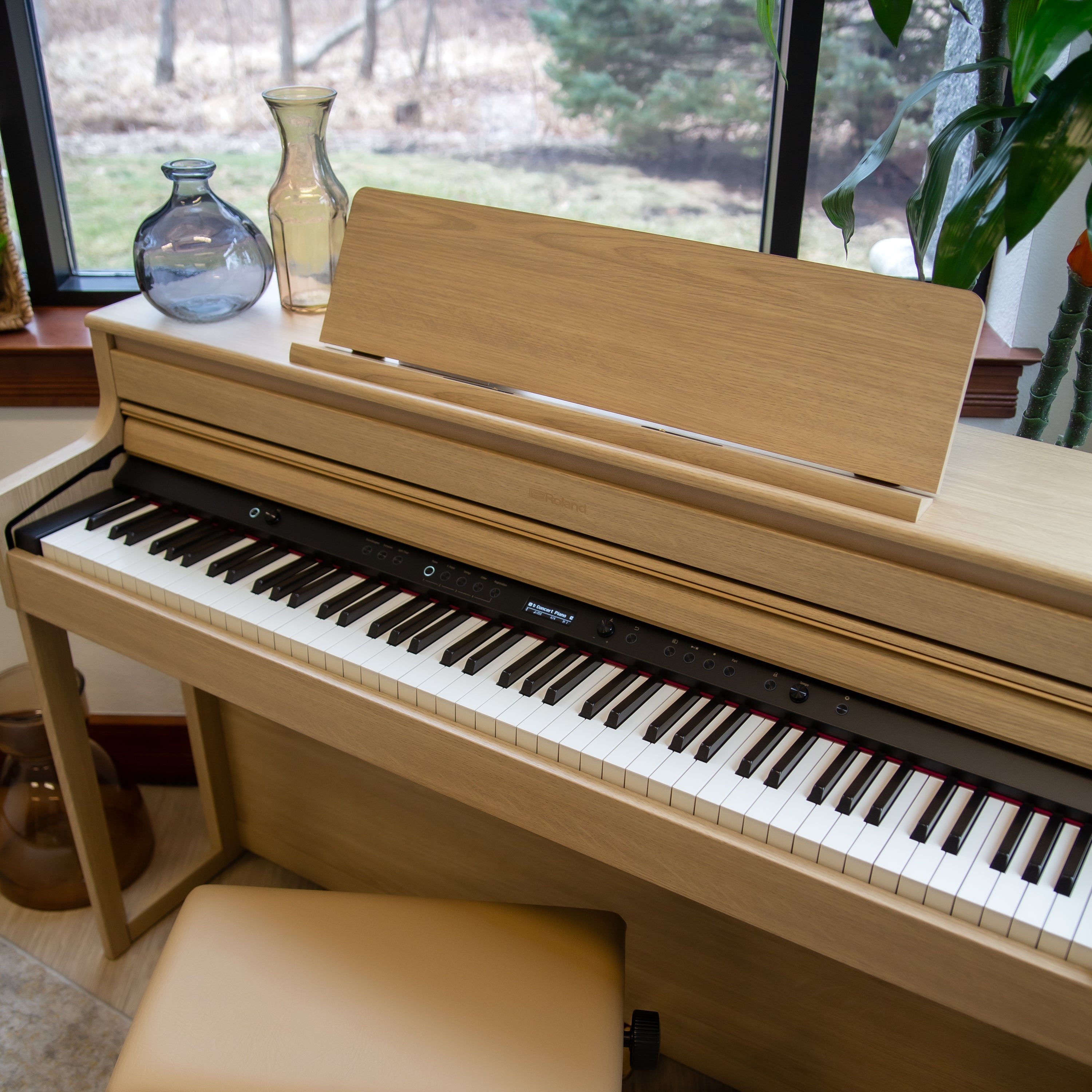 Roland HP704 Digital Piano - Light Oak with a bench in a room with large windows.