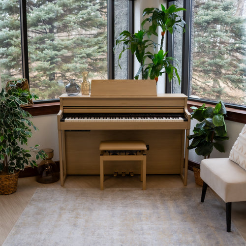 Roland HP704 Digital Piano - Light Oak in a room with large windows and potted plants