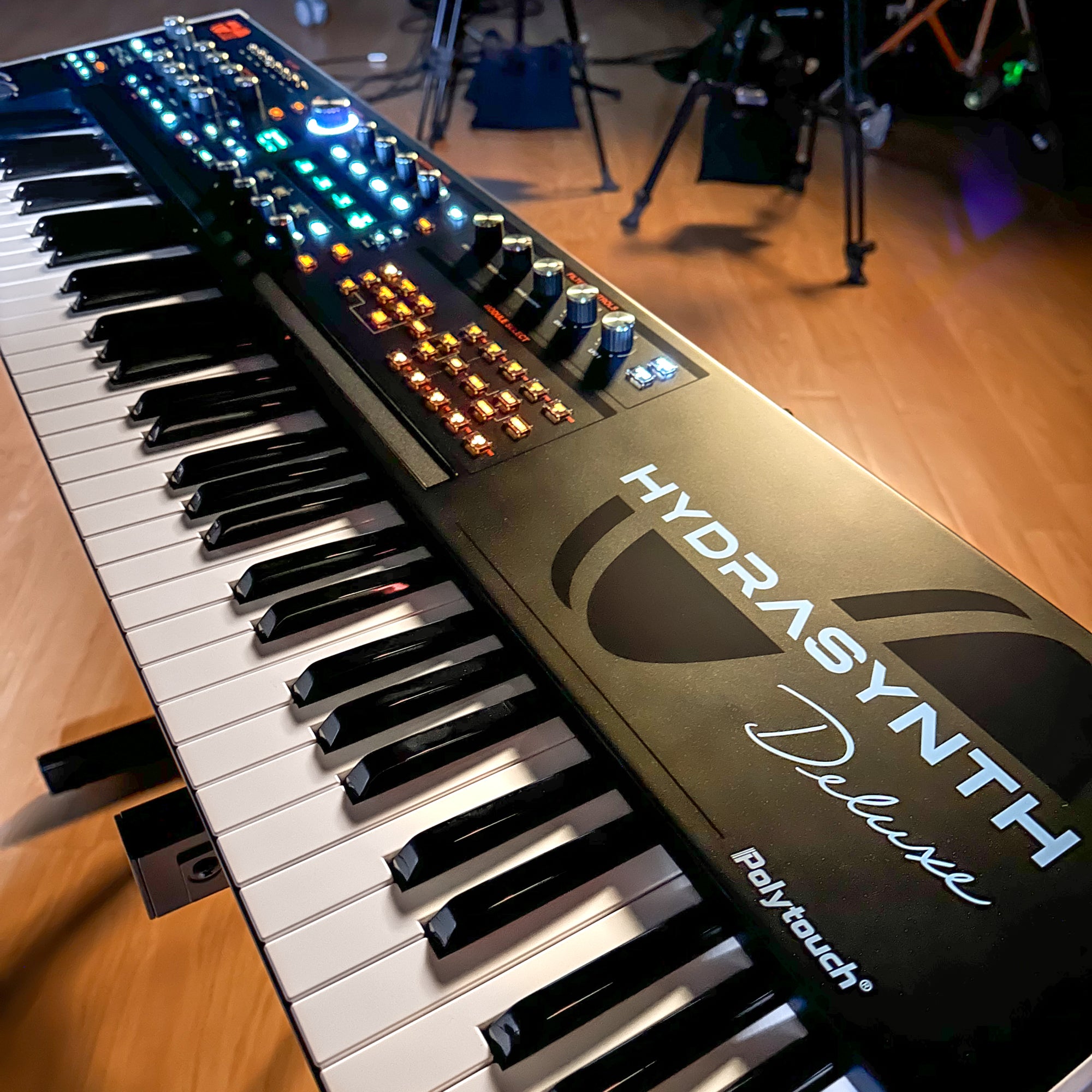ASM Hydrasynth Deluxe Polyphonic Wavemorphing Synthesizer, shown at an angle on a wooden floor, with its front panel controls and black-and-white keys visible.