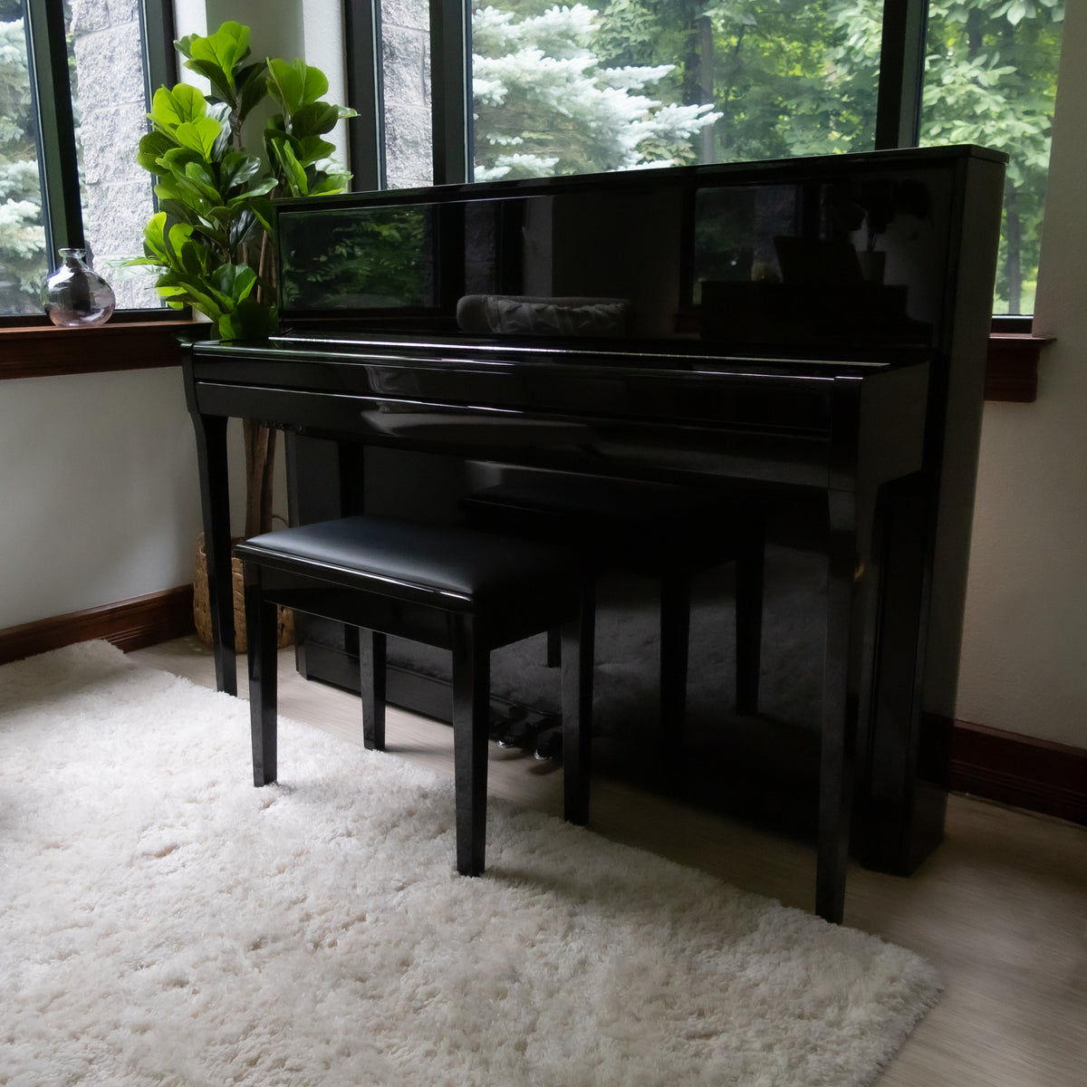 A Kawai NOVUS NV6 Hybrid Upright Piano with lid closed, placed in a room with large windows, a white shag rug, and a potted green plant.