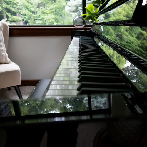 A close-up, angled view of a Kawai NOVUS NV6 Hybrid Upright Piano, set in a room with a window showing lush green trees outside.