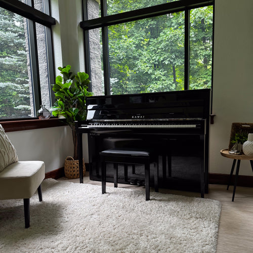 Kawai NOVUS NV6 Hybrid Upright Piano in a bright room with large windows, white shag rug, and green foliage outside.