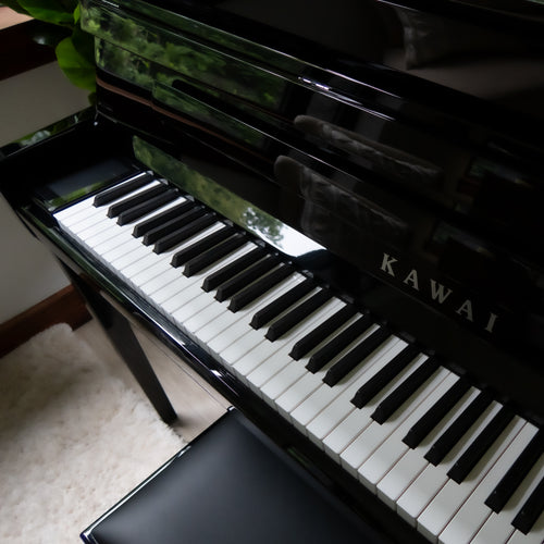 A Kawai NOVUS NV6 Hybrid Upright Piano shown at an angle, with the keyboard open and a matching black bench in front. The Kawai brand name is visible on the front.