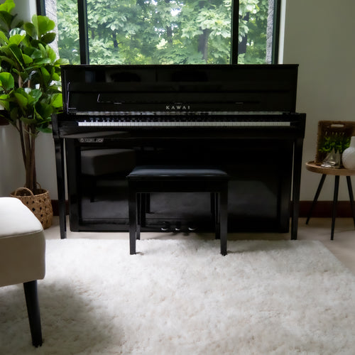 A Kawai NOVUS NV6 Hybrid Upright Piano, set in a bright room on a white shag rug with a window and green foliage in the background.