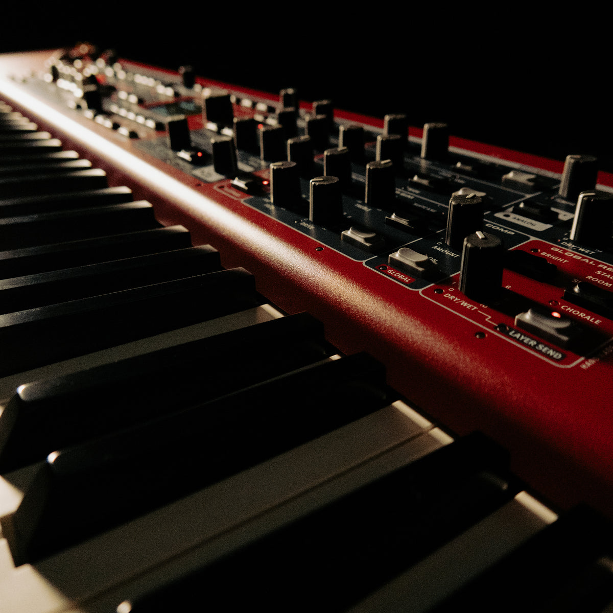 Close-up of a Nord Electro 7 with black and white keys and multiple black knobs, photographed in dramatic low light against a dark background.