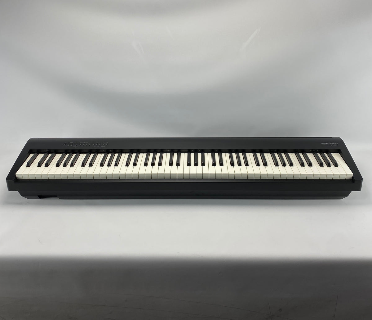 A Roland digital piano shown from the front against a neutral gray fabric backdrop.