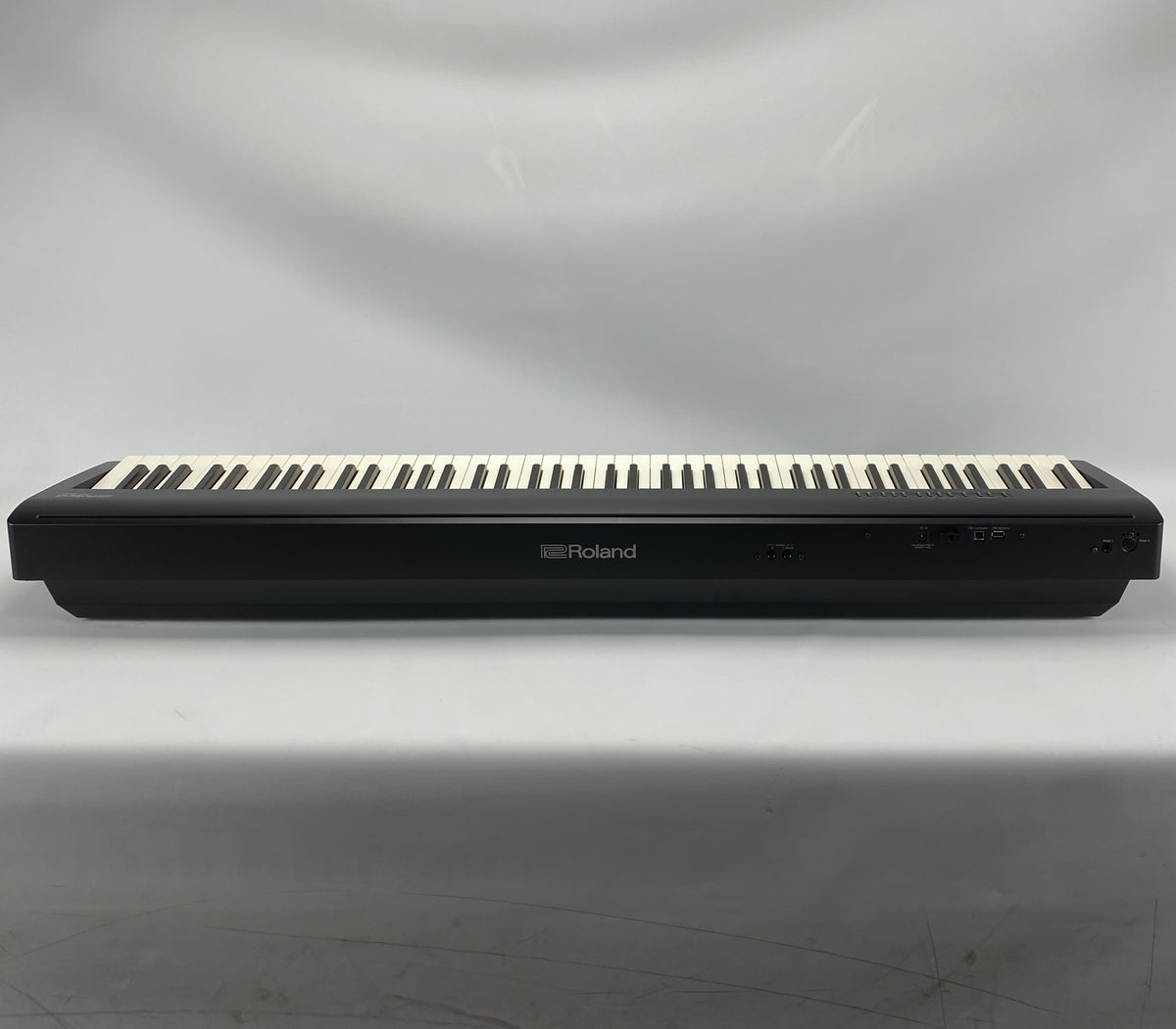 A Roland digital piano keyboard, shown from the back against a light gray draped fabric background.
