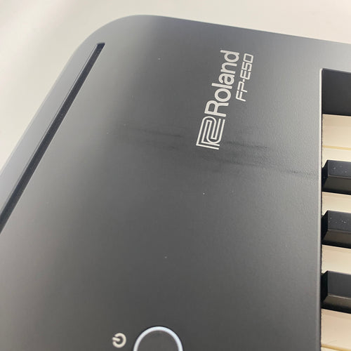 Angled close-up of Roland FP-E50 logo on right end of panel showing visible dark scuff marks