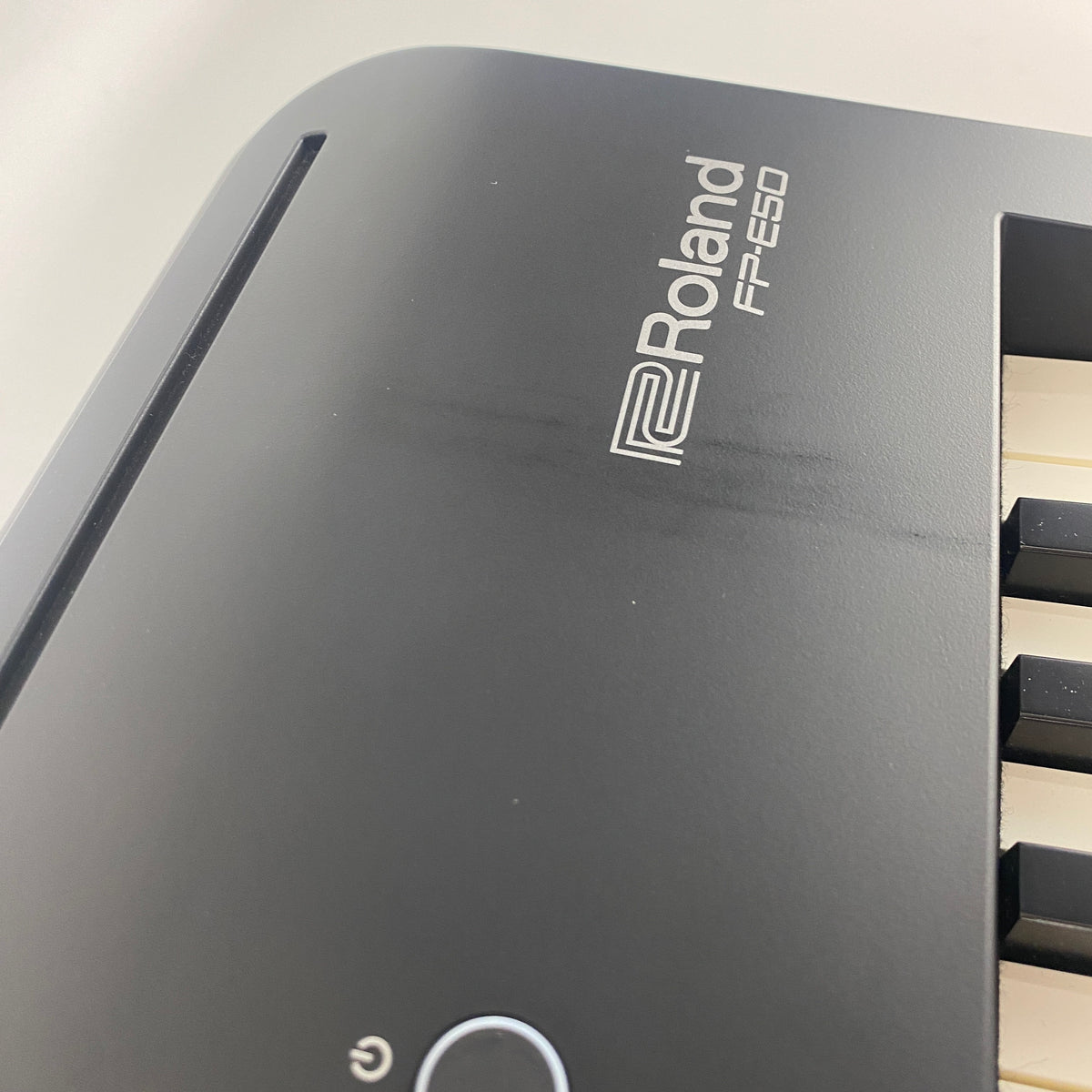 Angled close-up of Roland FP-E50 logo on right end of panel showing visible dark scuff marks