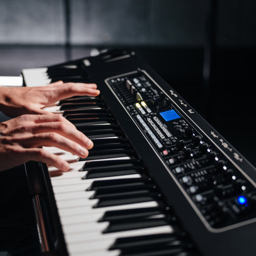 Close-up of hands playing the Yamaha CK76 semi-weighted keys, with the lit control panel and display beside them