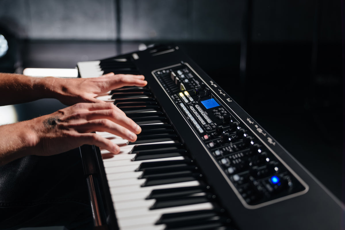 Close-up of hands playing the Yamaha CK76 semi-weighted keys, with the lit control panel and display beside them