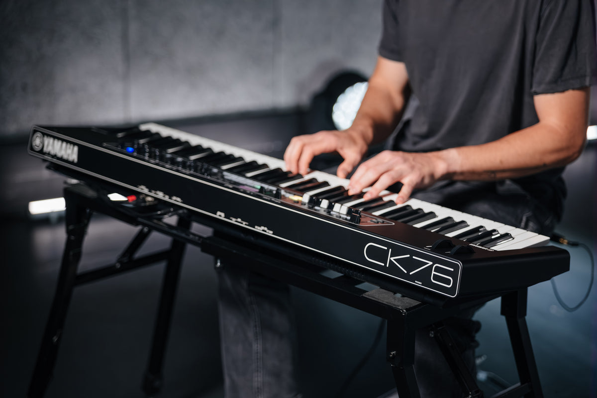 Musician playing the Yamaha CK76 stage keyboard on a stand, with the CK76 logo on the end panel in view