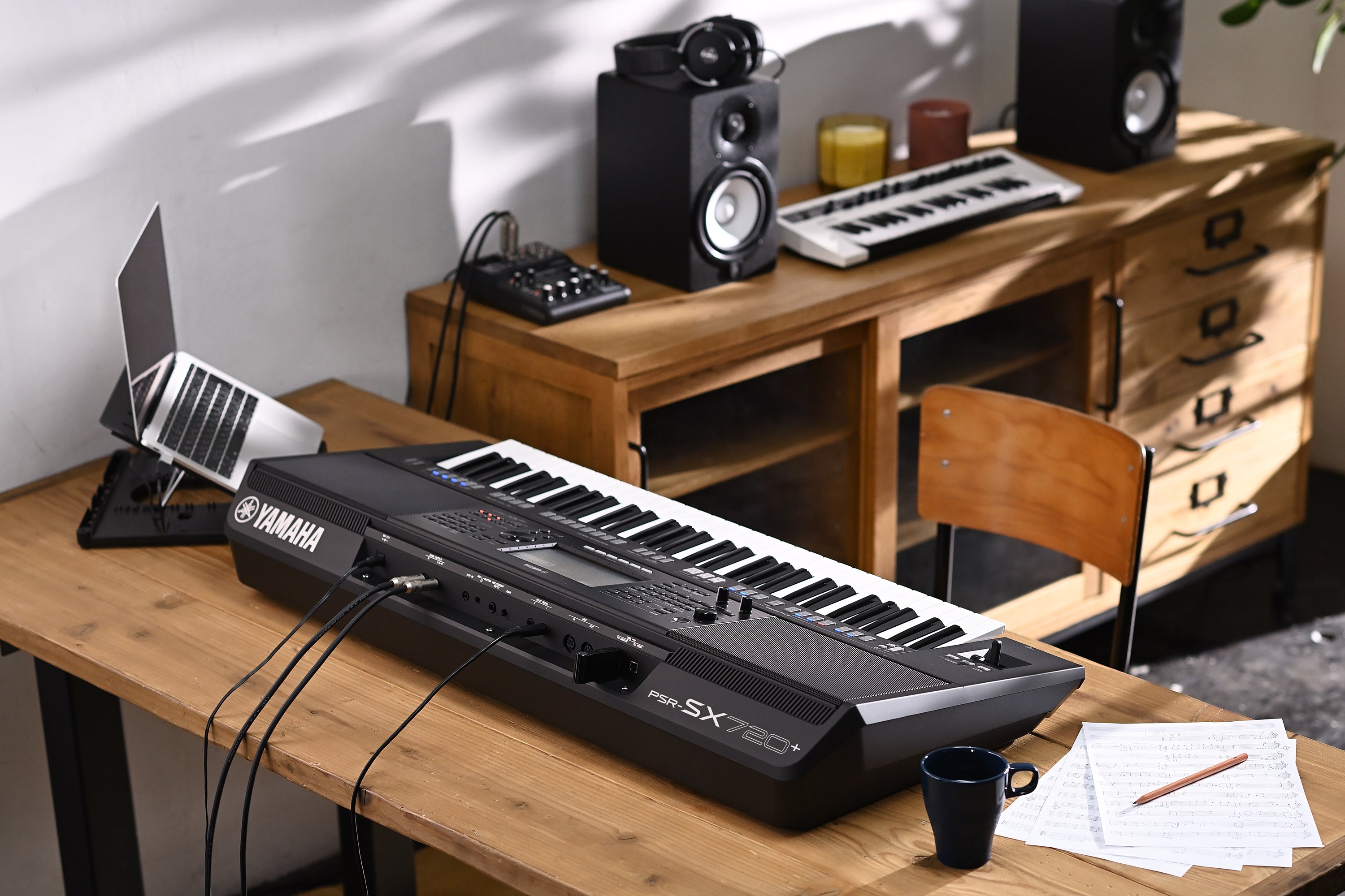 Yamaha keyboard on a wooden desk with laptop, speakers, and other music equipment.