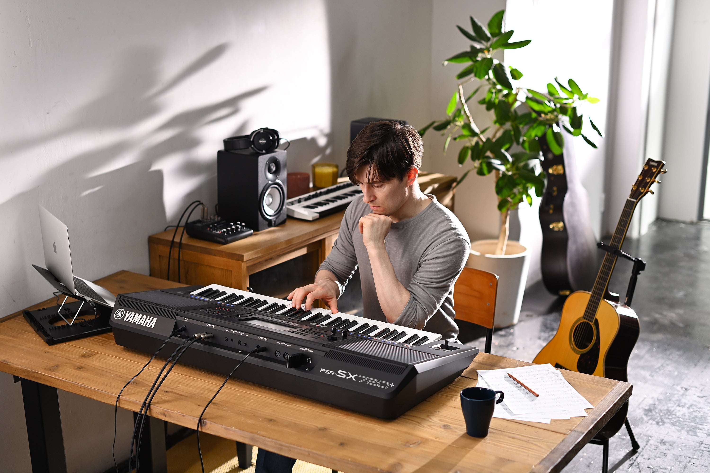 Person playing a Yamaha keyboard in a home studio setting with a laptop, speakers, and musical instruments.