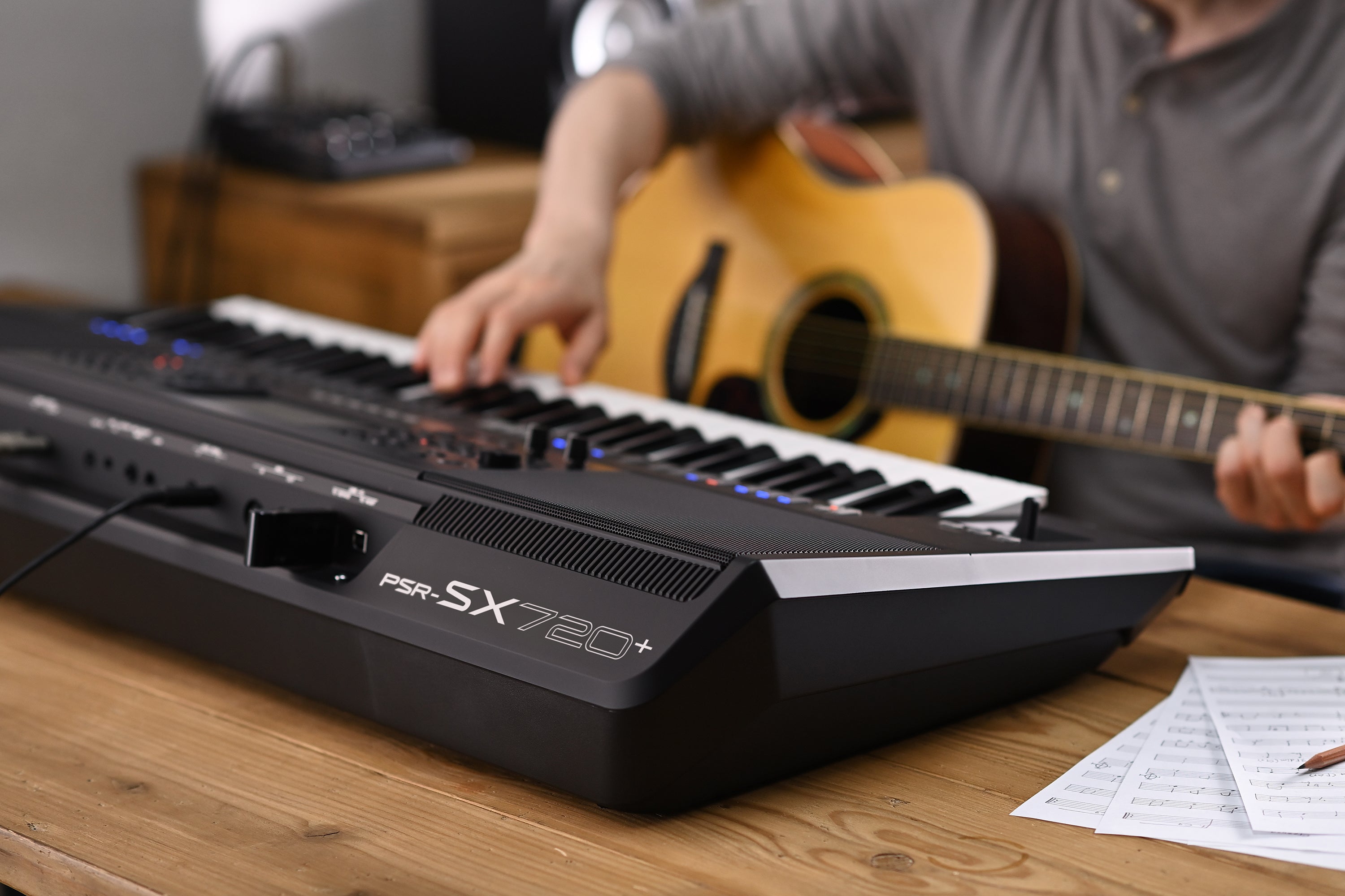 Keyboard on a wooden table with a person playing guitar in the background