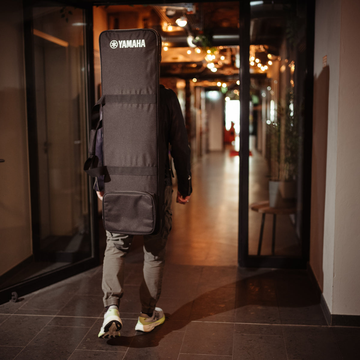 Lifestyle shot: Musician walking down a hallway carrying the Yamaha SCDE76 keyboard case backpack-style on their back