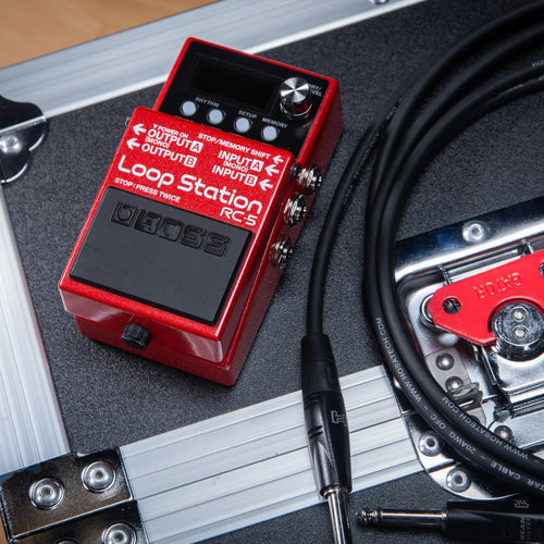 Top left angle view of the Boss RC-5 Loop Station sitting on the corner of a road case with a guitar cable coiled up next to it