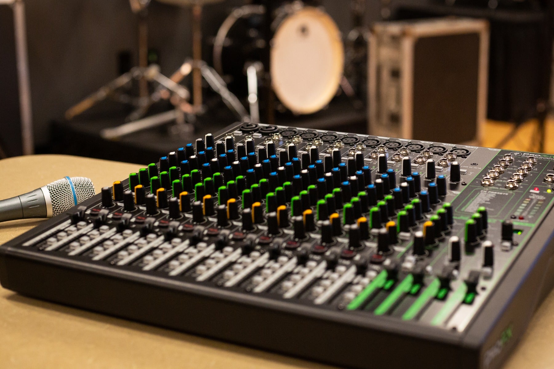 Right angle view of the Mackie ProFX16v3 Effects Mixer with USB on a work table at a gig with a microphone next to it