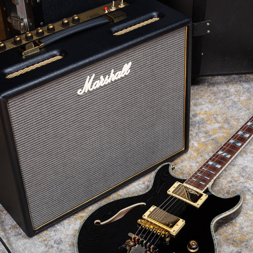 Top right angle view of the Marshall Origin20C 20W Tube Combo Amp on a rug with a guitar laying on the floor in front